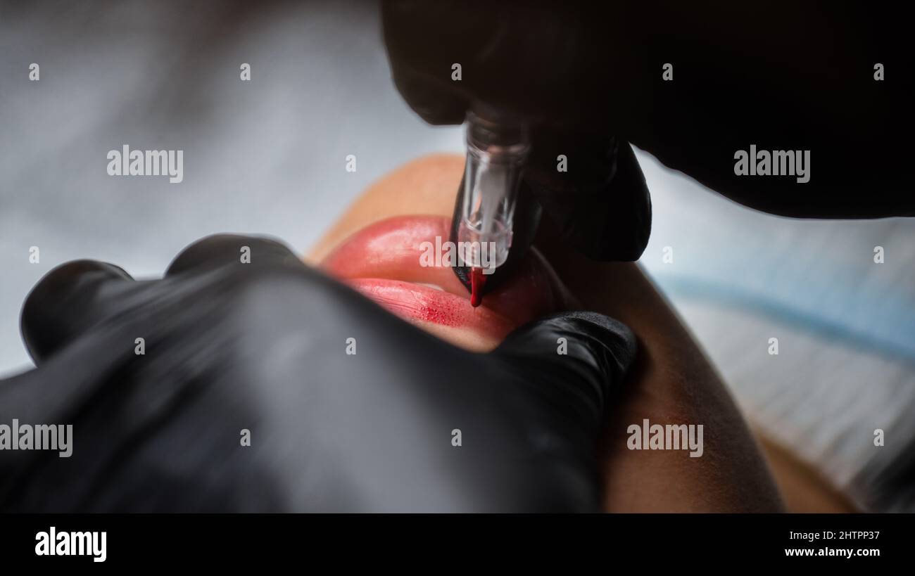 Cosmetologo in guanti neri makeup permanente sulle labbra della donna con tatuaggio penna macchina. Processo di microblading Foto Stock
