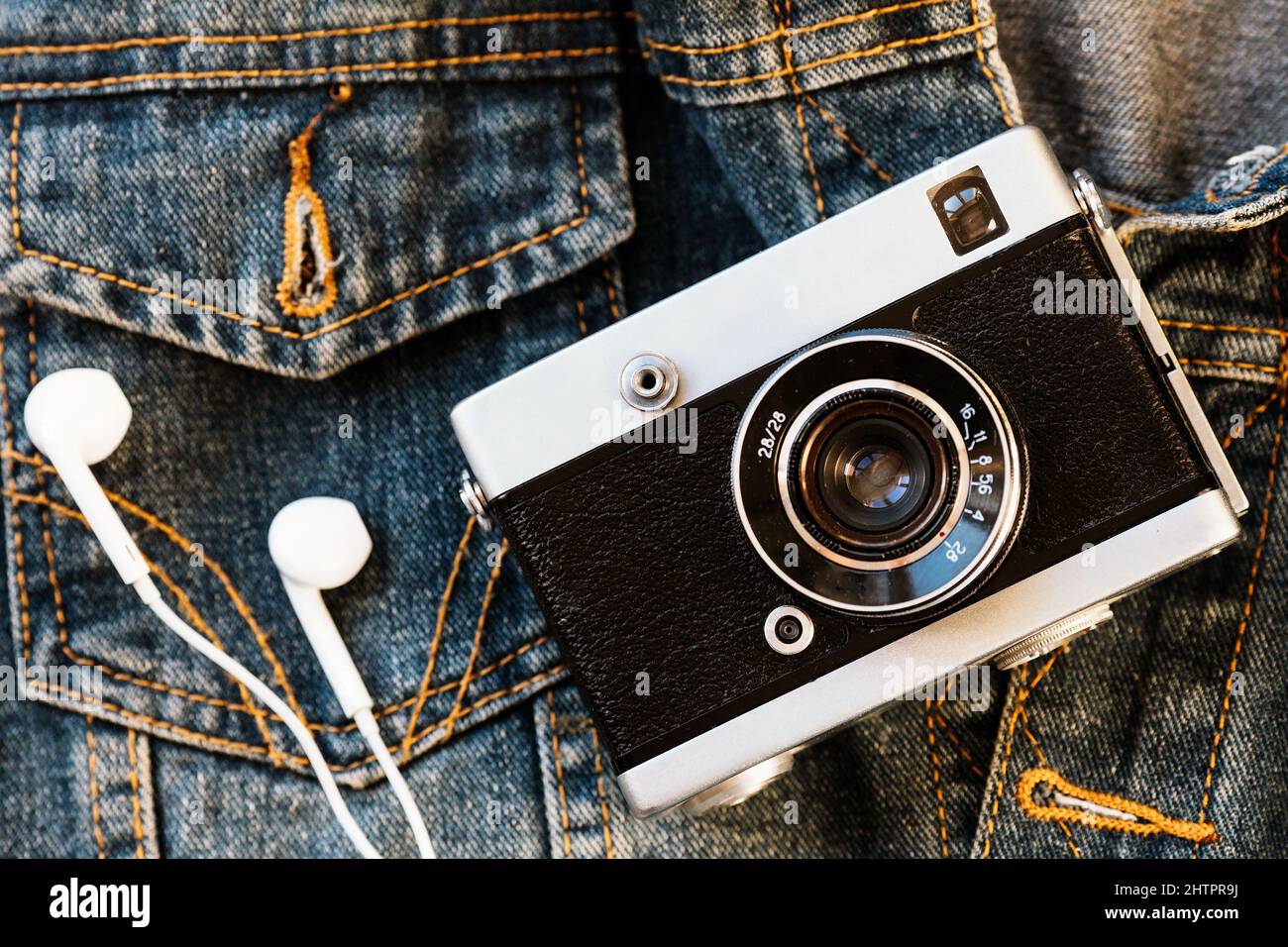 La videocamera e le cuffie bianche con cavo si appoggiano sullo sfondo del denim. Sfondo hipster alla moda. Stile retrò. Giornata del fotografo. Vista dall'alto Foto Stock
