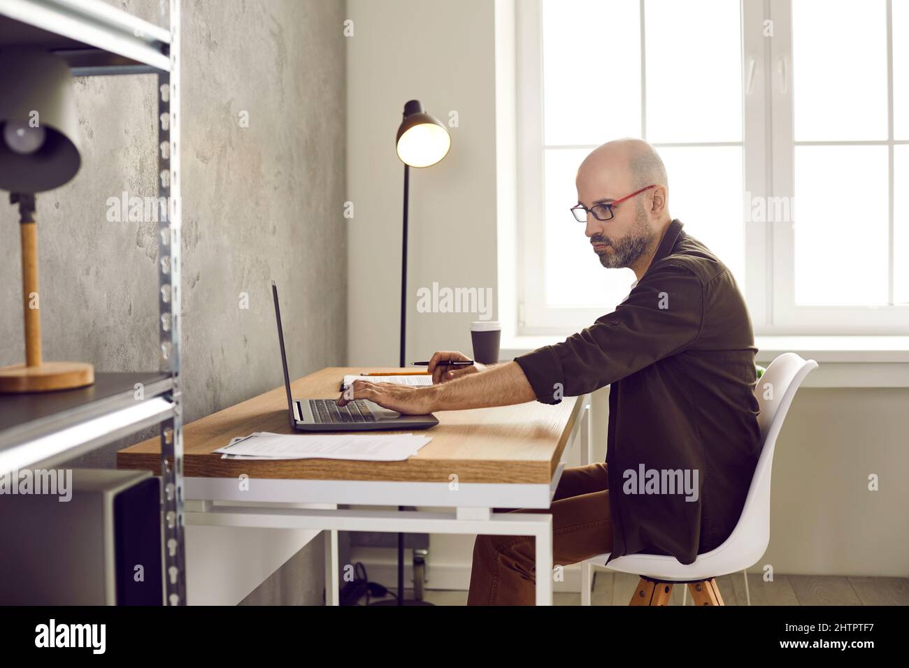 Uomo d'affari adulto concentrato e serio che lavora con documenti e notebook in ufficio. Foto Stock