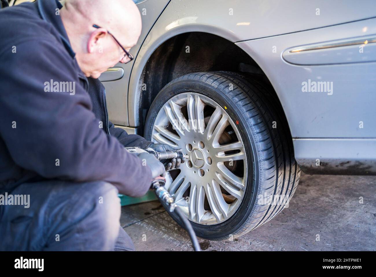 Officina di garage per pneumatici nel Regno Unito, specialista di pneumatici: Meccanico di officina isolato che monta una ruota su un'auto utilizzando una chiave pneumatica. Foto Stock