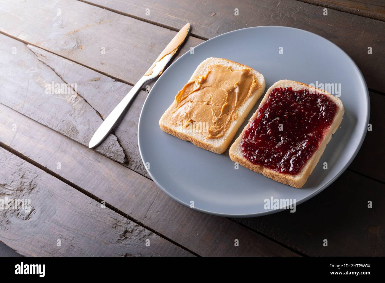 Vista ad angolo alto del burro di arachidi a faccia aperta e sandwich di gelatina in piastra sul tavolo con coltello da tavolo Foto Stock