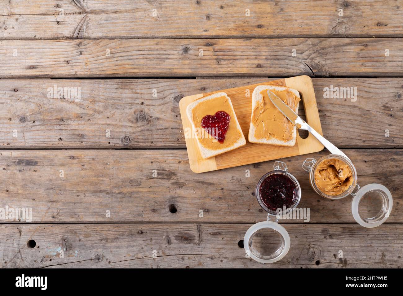Vista dall'alto del burro di arachidi a faccia aperta e sandwich di gelatina sul bordo di servizio con vasetti al tavolo Foto Stock