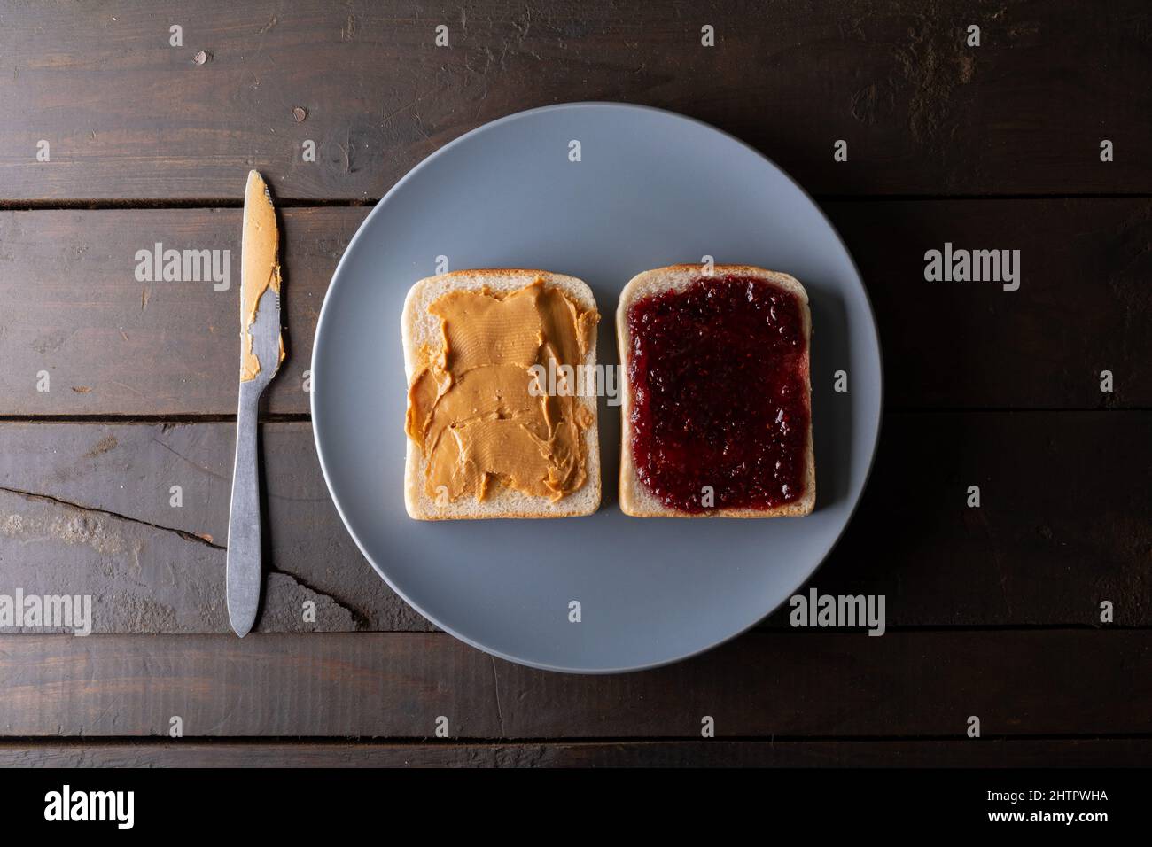 Direttamente sopra il colpo di burro di arachidi faccia aperta e sandwich di gelatina in piastra sul tavolo con il coltello da tavolo Foto Stock