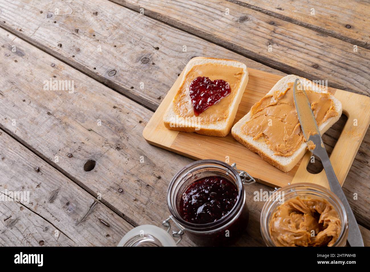 Vista ad angolo alto del burro di arachidi a faccia aperta e sandwich di gelatina sul bordo di servizio con vasetti al tavolo Foto Stock