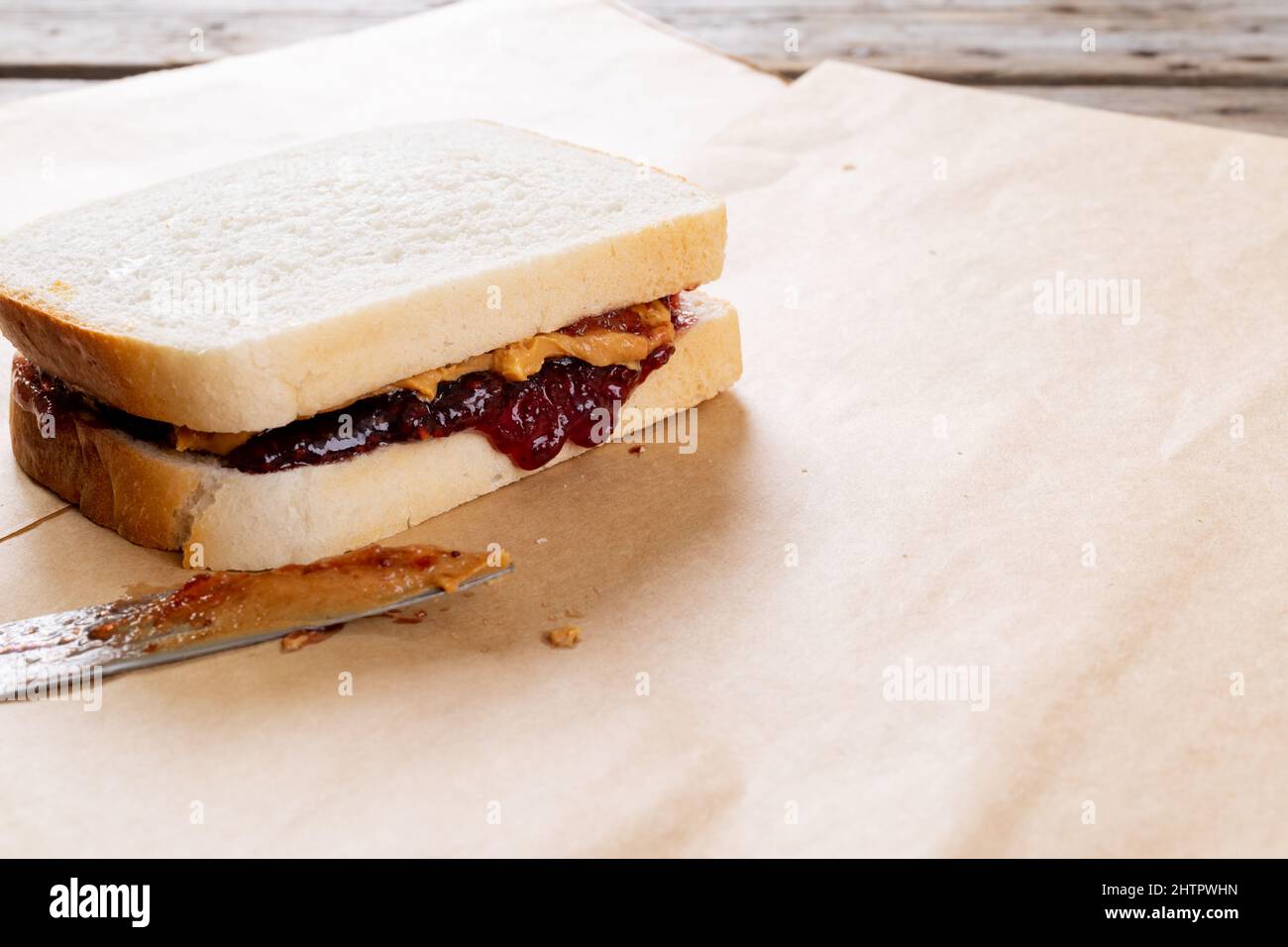 Primo piano del burro di arachidi e sandwich di gelatina su carta marrone con il coltello da tavolo a tavola Foto Stock