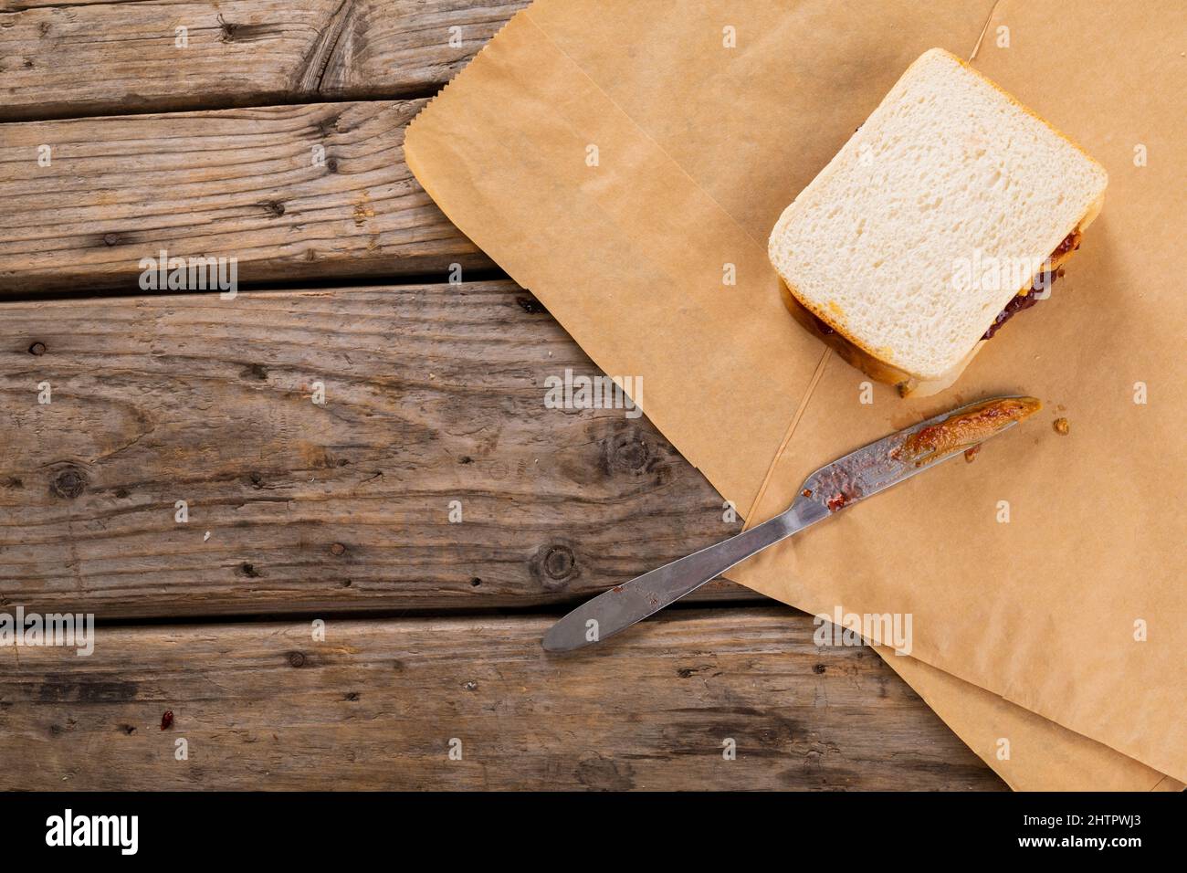 Vista ad angolo alto del burro di arachidi e dei sandwich di gelatina con il coltello da tavolo su carta marrone al tavolo Foto Stock