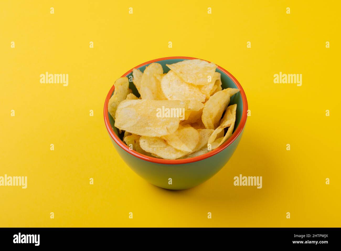 Primo piano ad angolo elevato delle patatine in un recipiente verde su sfondo giallo Foto Stock