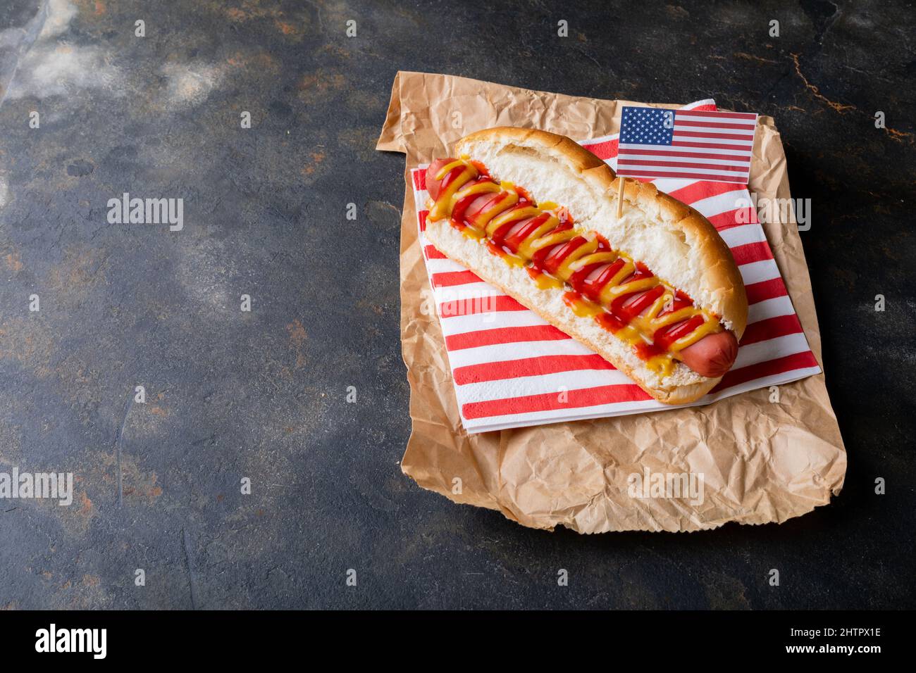 Bandiera americana su hot dog con salsa di pomodoro e mostered su carta di cera marrone a tavola Foto Stock