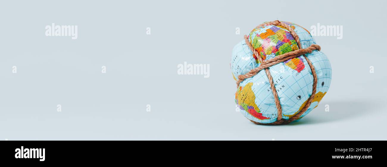 un globo di terra flessibile strettamente legato con corda su sfondo blu pallido, in un formato panoramico da usare come banner web o intestazione Foto Stock