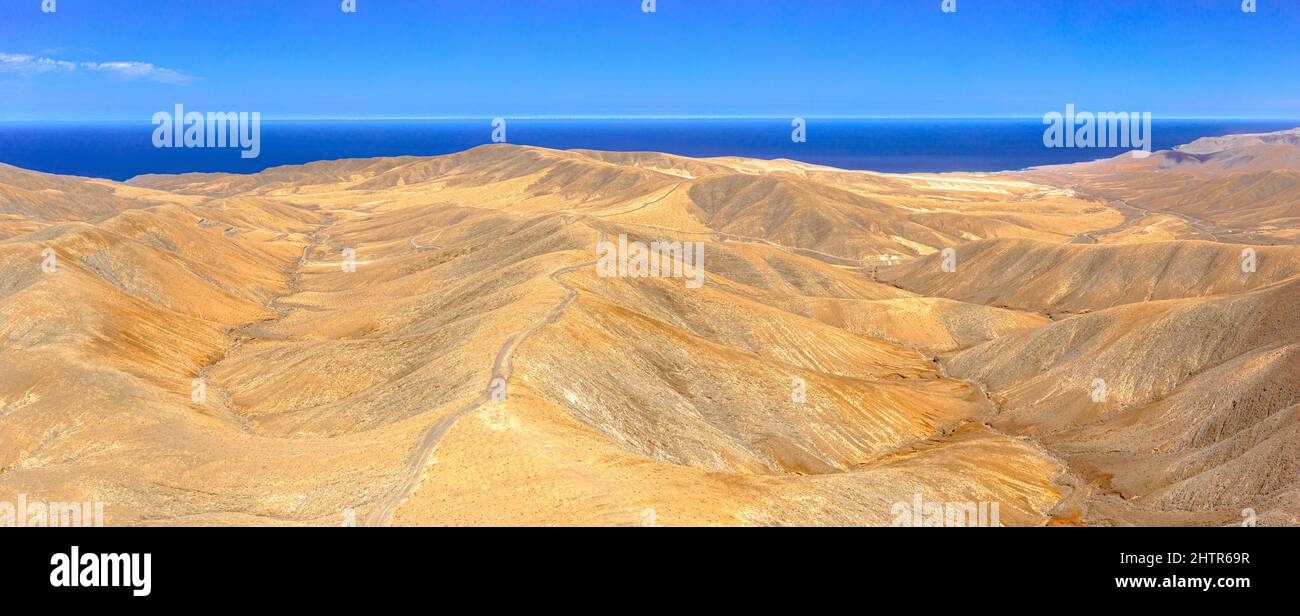 Vista aerea della strada vuota che attraversa le montagne del deserto verso l'Oceano Atlantico blu, Fuerteventura, Isole Canarie, Spagna Foto Stock