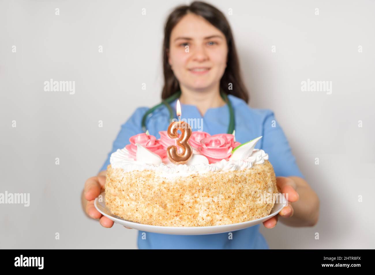 Il medico o l'infermiere tiene una torta di compleanno con il numero tre per l'anniversario dell'apertura della clinica Foto Stock