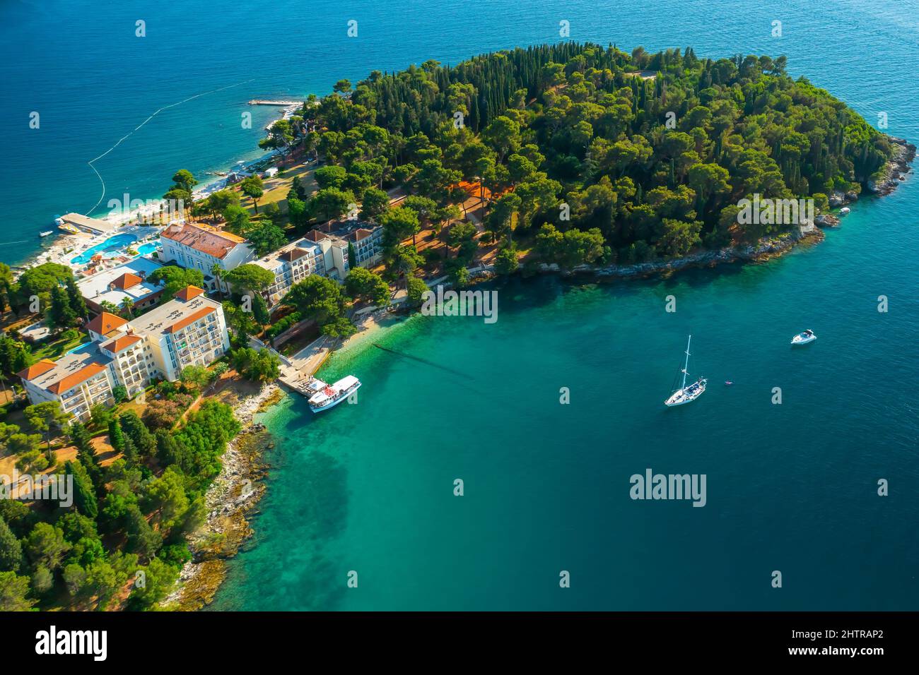 Edifici con tetti rossi sulla penisola con foresta verde vicino al mare Adriatico. Barche che si sgocciolano sulla superficie dell'acqua calma vicino alla città croata. Panorama aereo Foto Stock