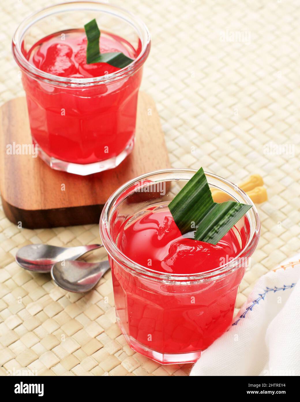 Manisan Kolang-Kaling (frutti di palma di zucchero conservati) di colore rosso. Servito in un bicchiere con Coaster di legno e foglie di Pandan come guarnitura. Foto Stock