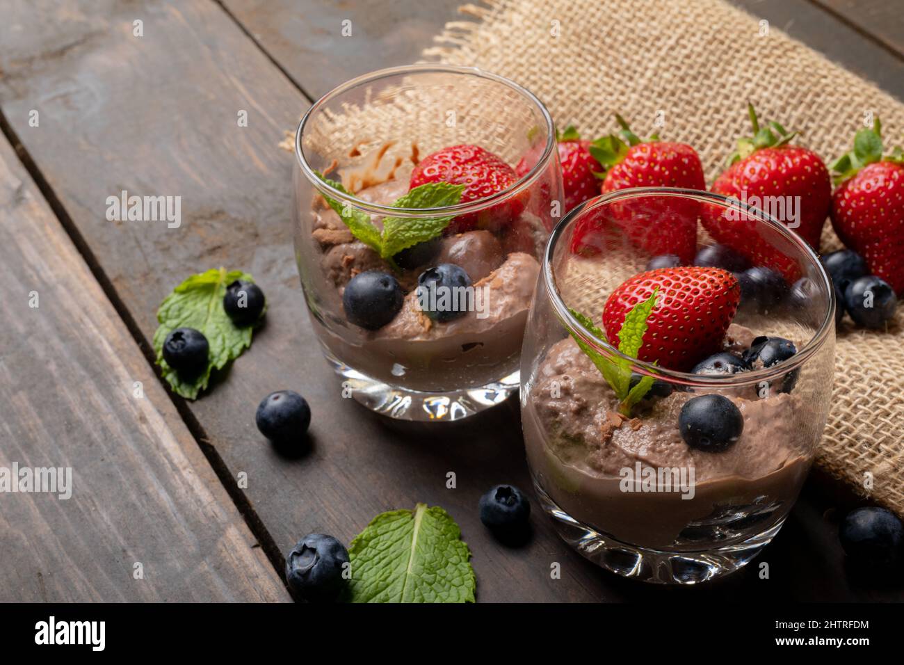 Primo piano di mousse al cioccolato con fragole, mirtilli e foglie di menta serviti in bicchieri Foto Stock