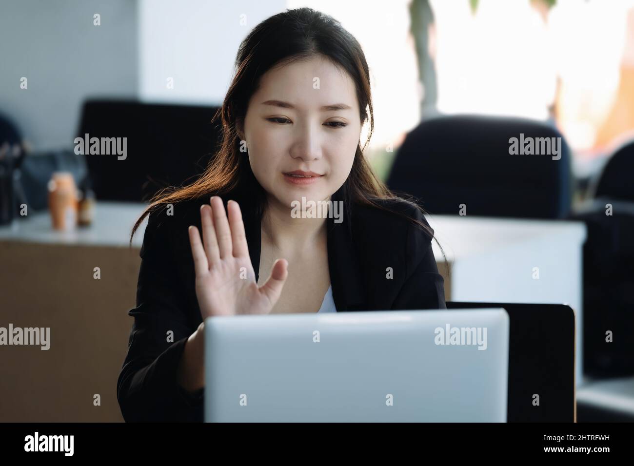Una donna asiatica o un uomo d'affari sorride e si sta muovendo verso un collega che utilizza un notebook tramite videoconferenza. Foto Stock