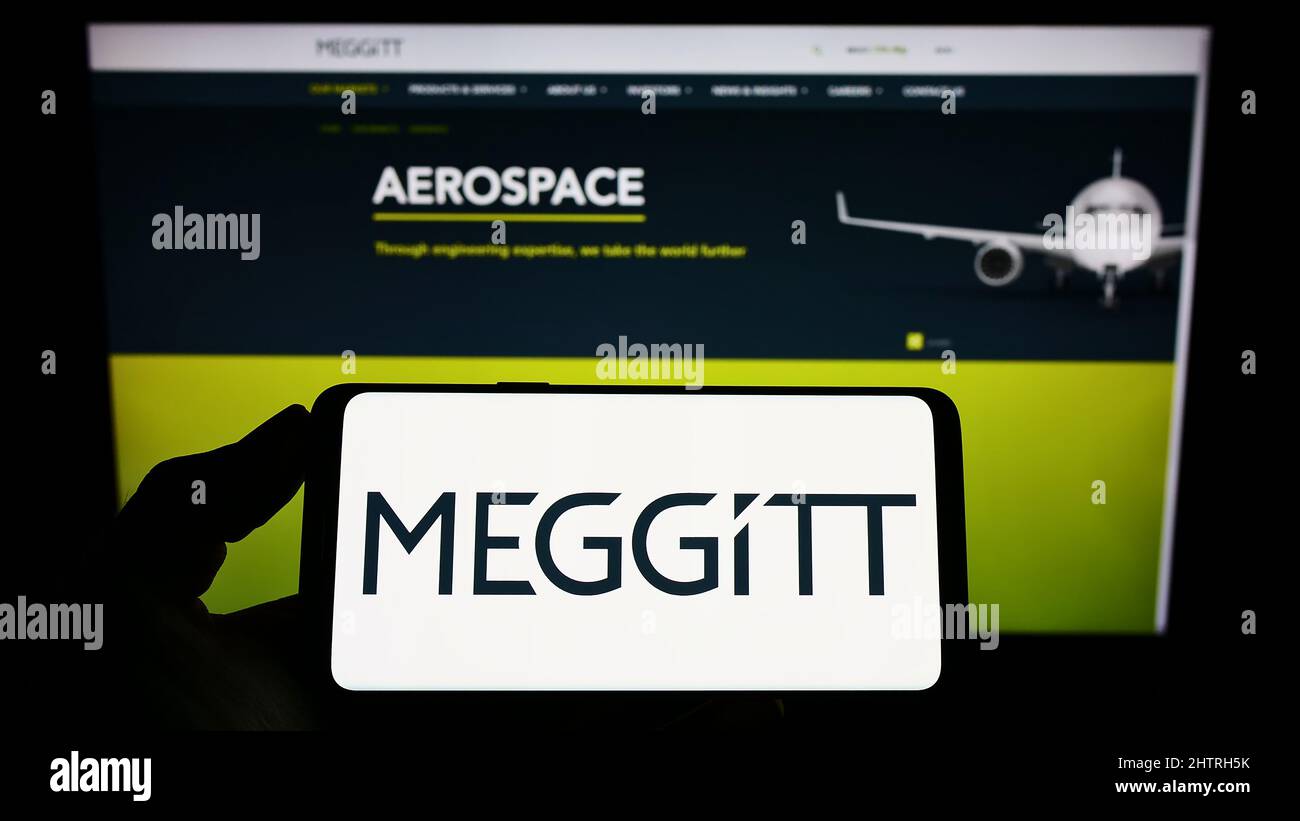 Persona che tiene smartphone con il logo della società aerospaziale britannica Meggitt plc sullo schermo di fronte al sito web. Mettere a fuoco sul display del telefono. Foto Stock