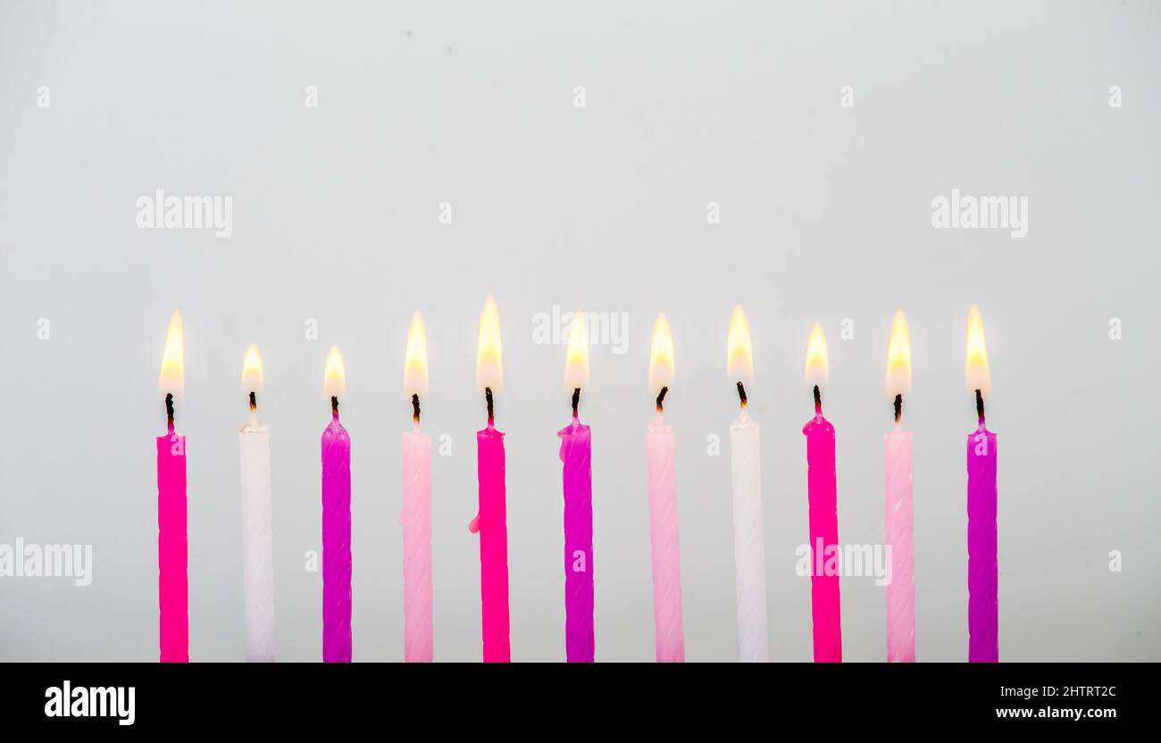 Varie candele di torta di compleanno di colore rosa che bruciano in linea su sfondo grigio, scatto studio, molto spazio di copia per i saluti. Vista laterale. Foto Stock