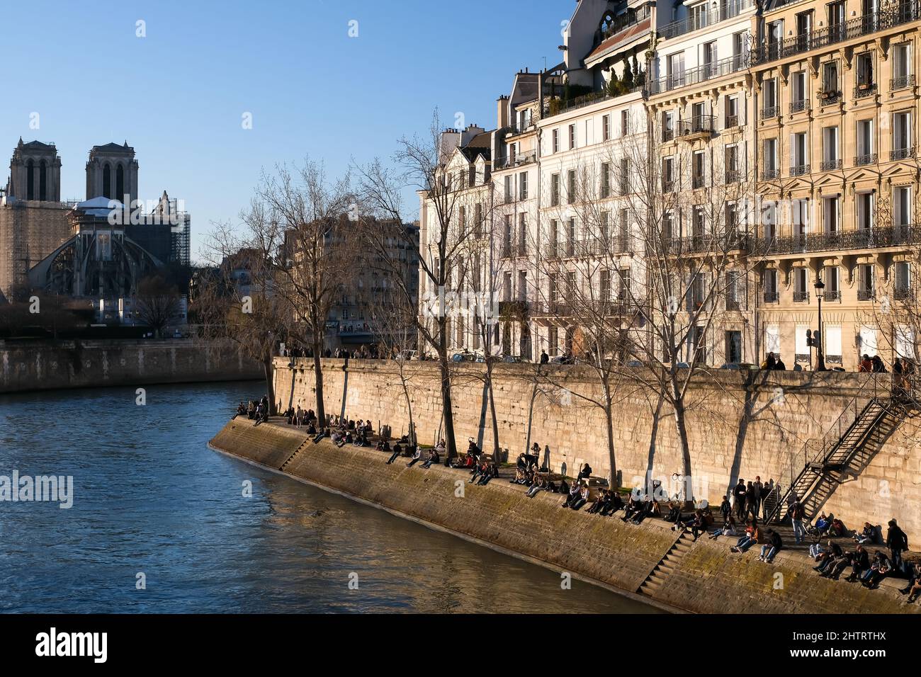 La gente si siede e si gode la giornata di sole accanto al fiume Senna nel pittoresco centro di Parigi Foto Stock