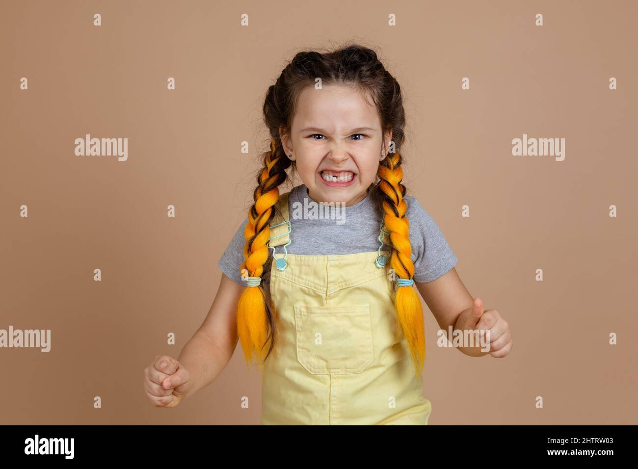 Giocoso indulgere bambina con pigtail kanekalon giallo, spaventoso gente con denti ardati con dente mancante che indossa jumpsuit giallo e grigio Foto Stock