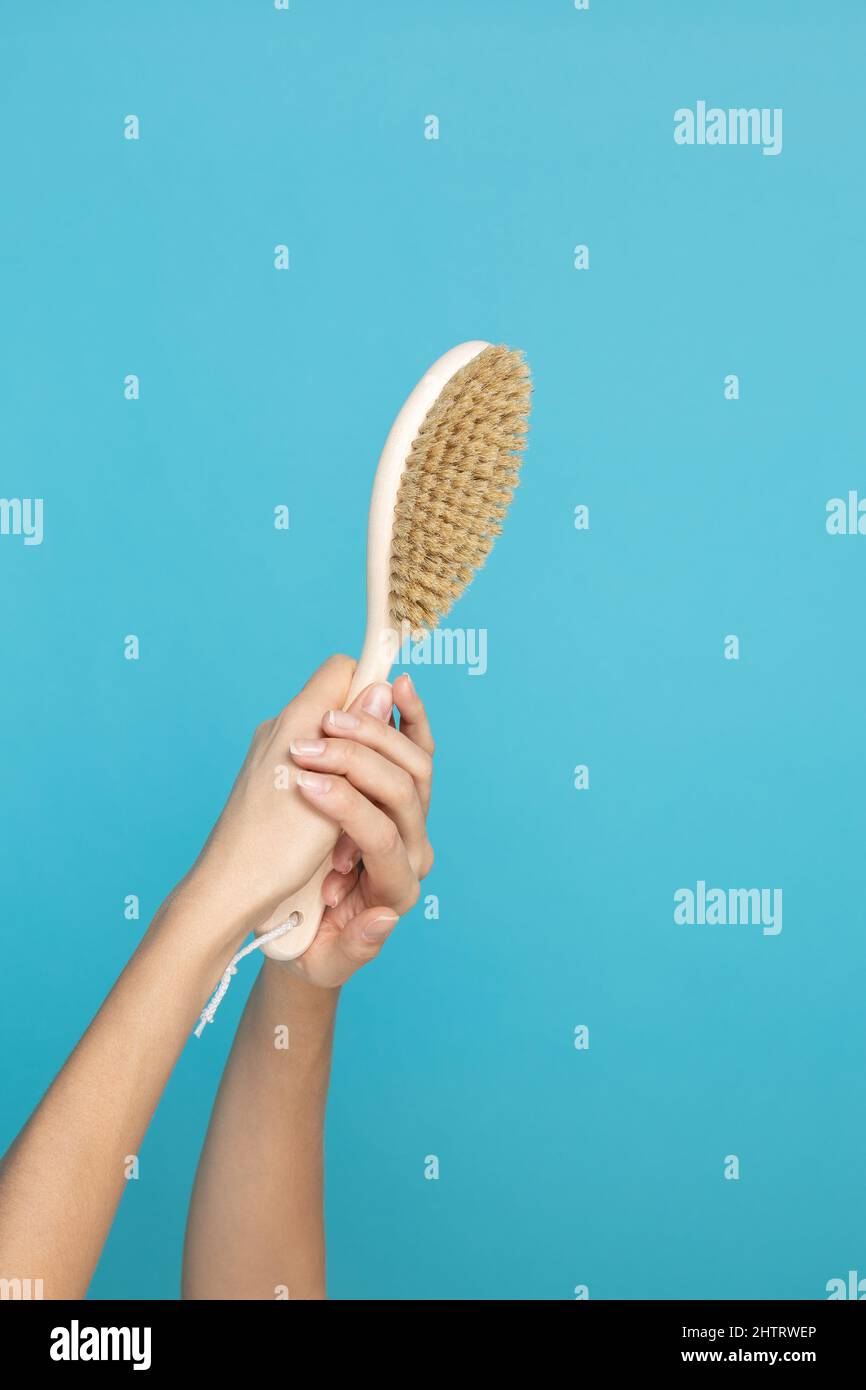 Spazzola in legno per massaggio della pelle asciutta con le mani su sfondo blu. Cura di sé e cura del corpo. Procedure anticellulite che mirano a sbarazzarsi di Foto Stock
