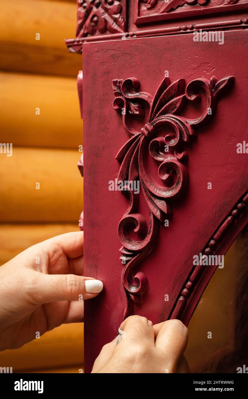 Le mani femminili preparano cartone rosso pronto per incollare nuovi ornamenti intagliati in officina per il restauro di mobili. Riutilizzo. Dare nuova vita al vecchio Foto Stock