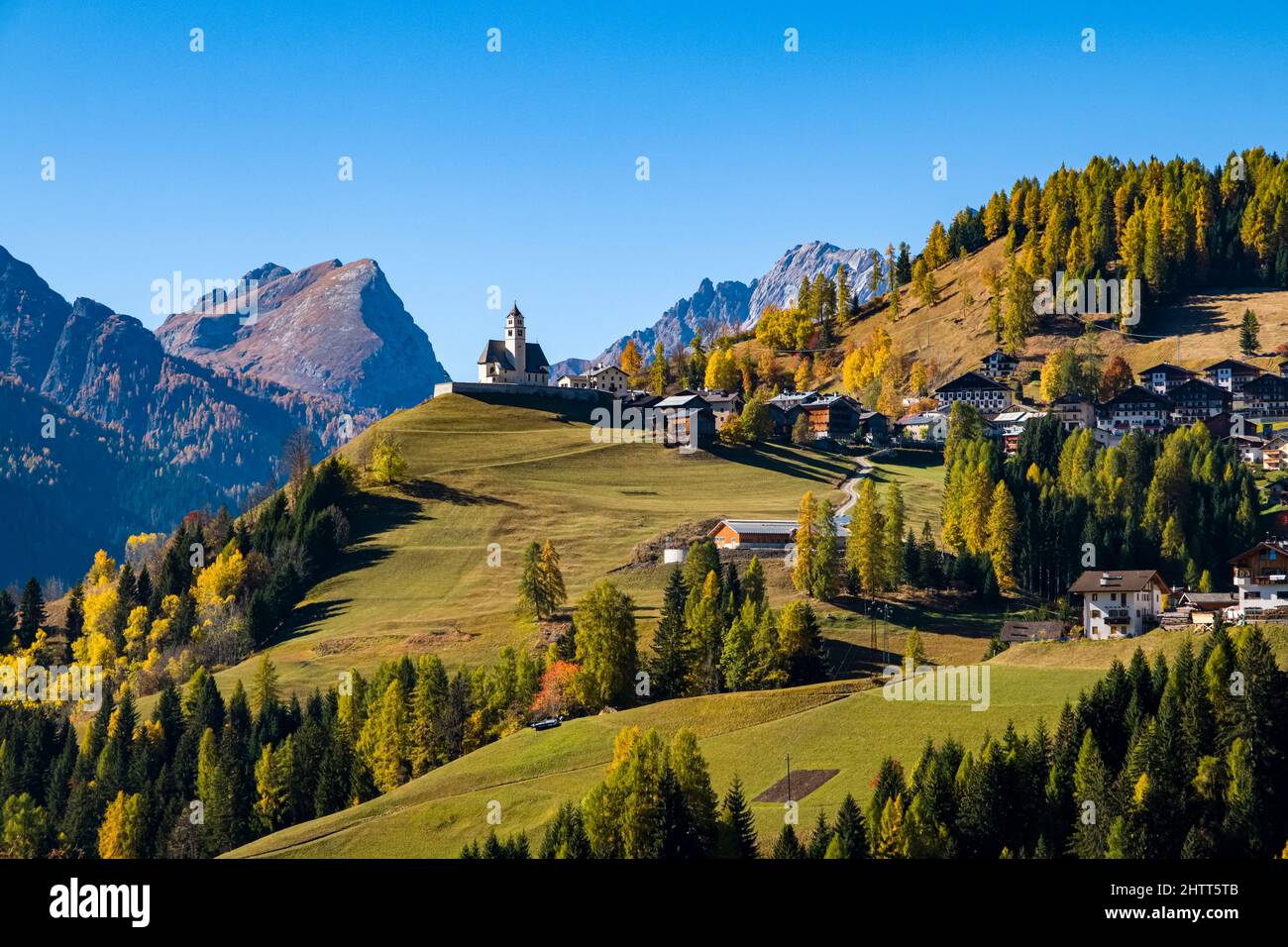 Case e chiesa del villaggio Colle Santa Lucia, circondato da larici e pini colorati in autunno, Dolomiti montagne in lontananza. Foto Stock