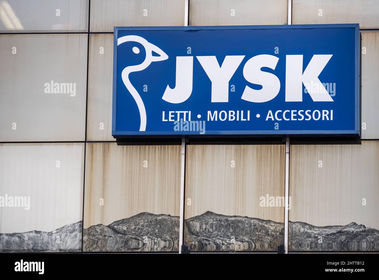 Locarno, Svizzera - 29 dicembre 2021: Un segno per mobili gigante Jysk sulla facciata di vetro con montagne sotto il segno come un riflesso nel wal Foto Stock