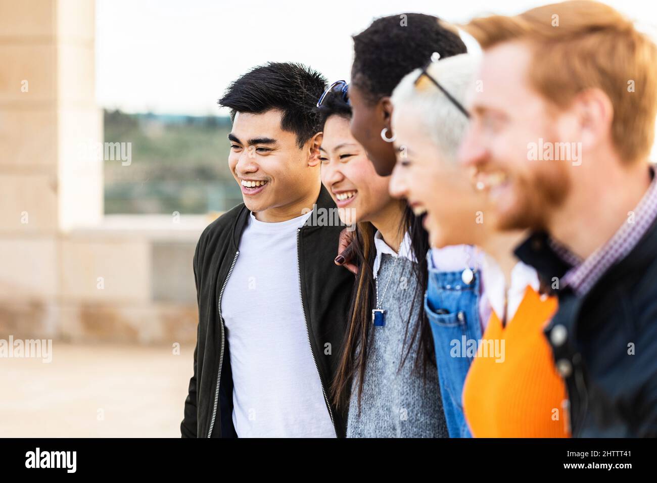 Un gruppo diversificato di giovani amici uniti che ridono insieme all'aperto Foto Stock