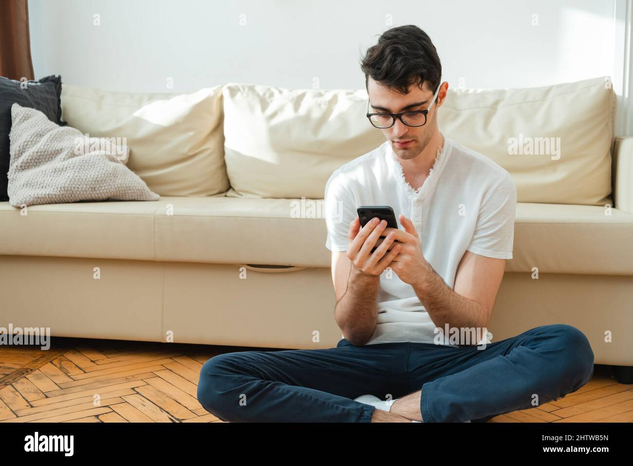 Ritratto di un freelance maschile che è sempre in contatto a casa. Bell'uomo ha messo a fuoco il suo smartphone mentre si siede sul divano. Foto Stock
