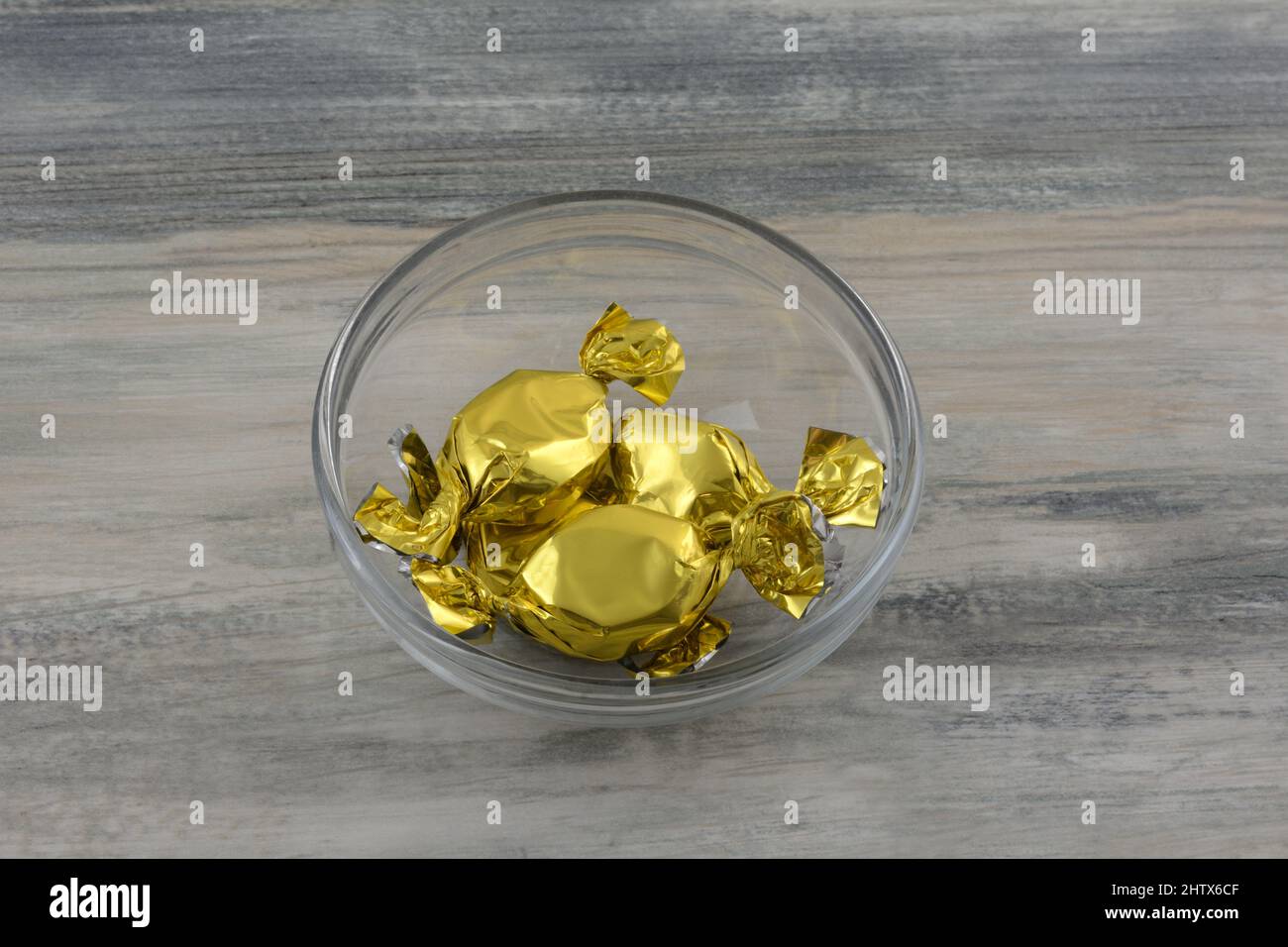Caramelle caramelle in oro avvolgenti in ciotola di vetro Foto Stock