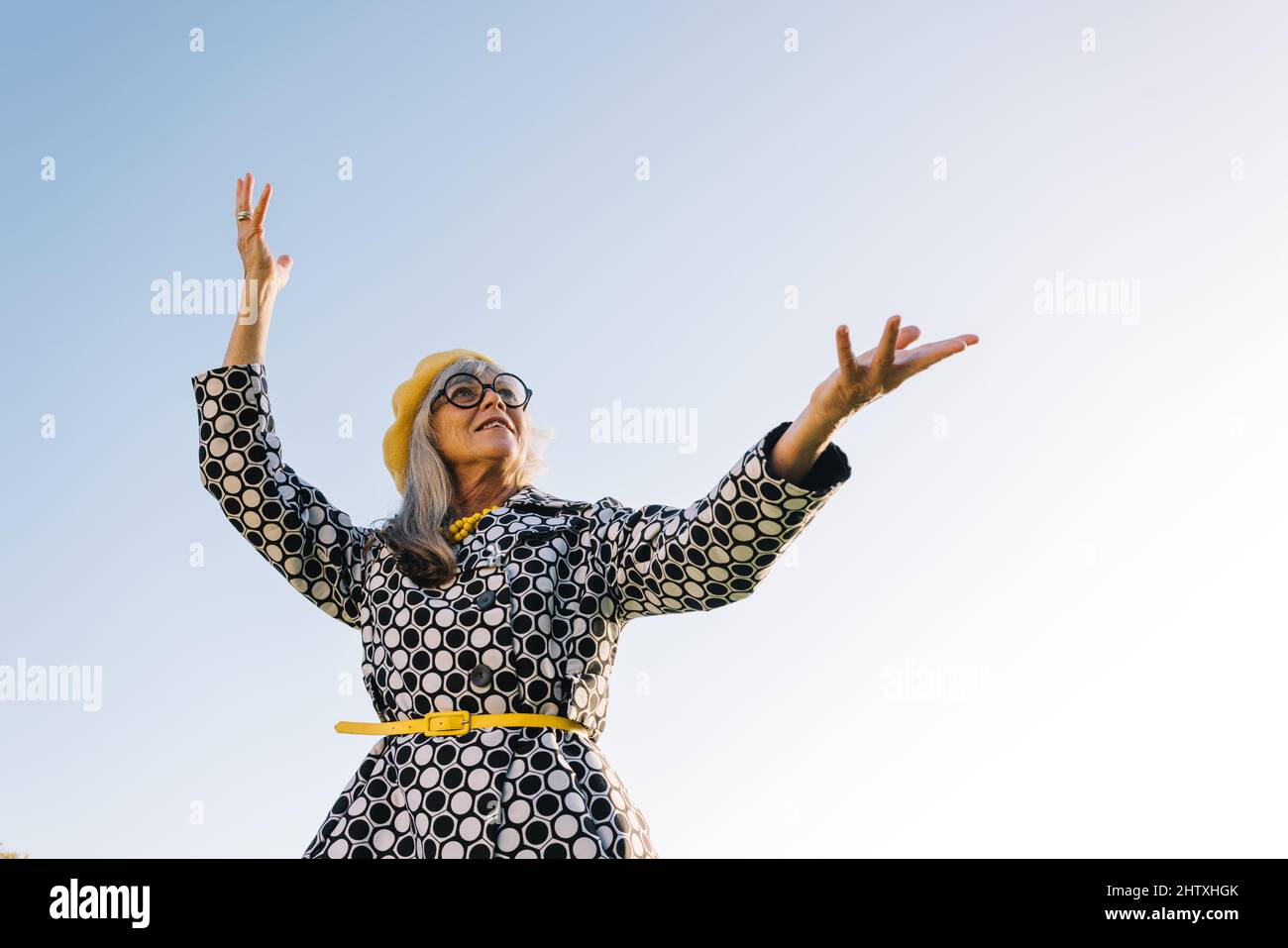 Donna anziana spensierata che solleva le mani in festa all'aperto. Donna anziana beatful che indossa abiti casual colorati in estate. Tappeto allegro Foto Stock