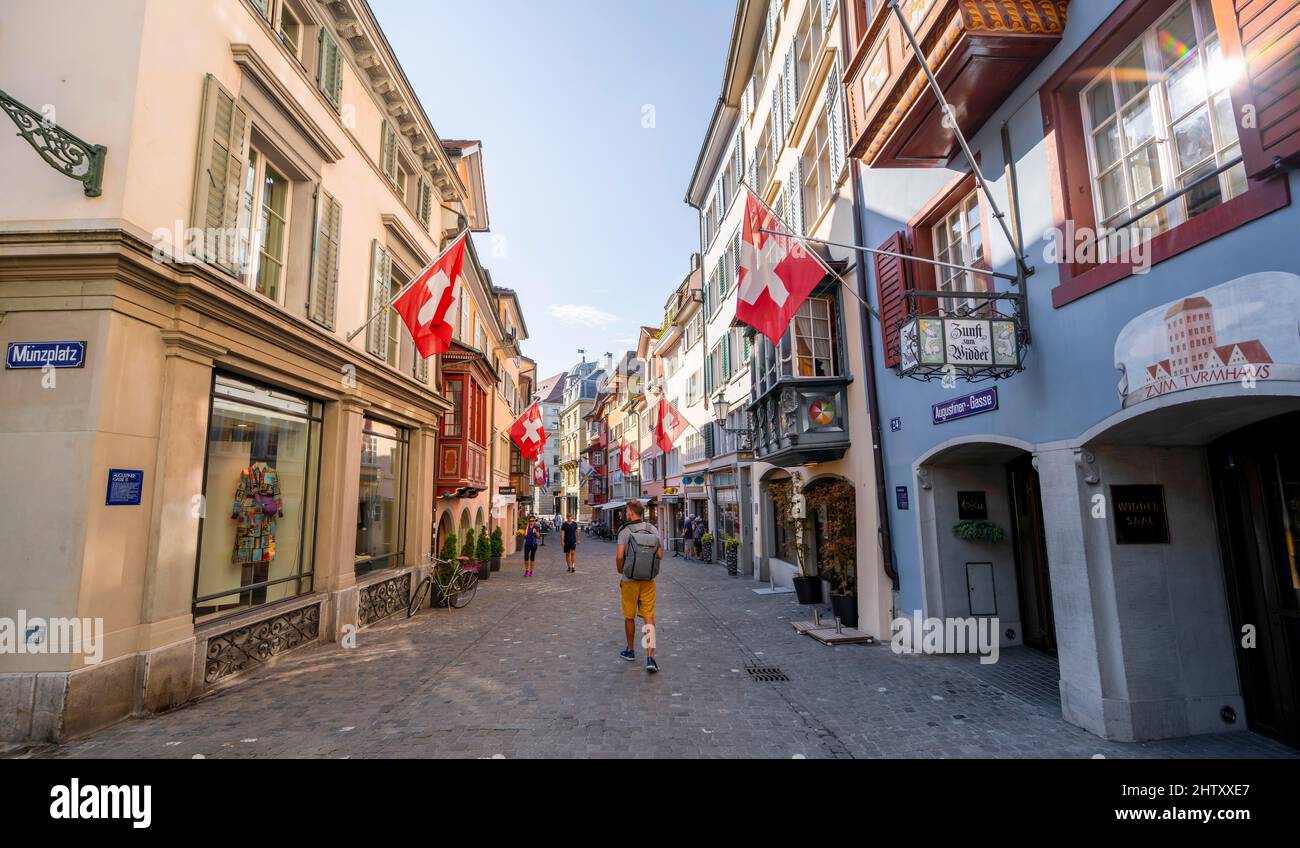 Turista in Augustinergasse, vicolo con case storiche e bandiere svizzere nel centro storico, Zurigo, Svizzera Foto Stock