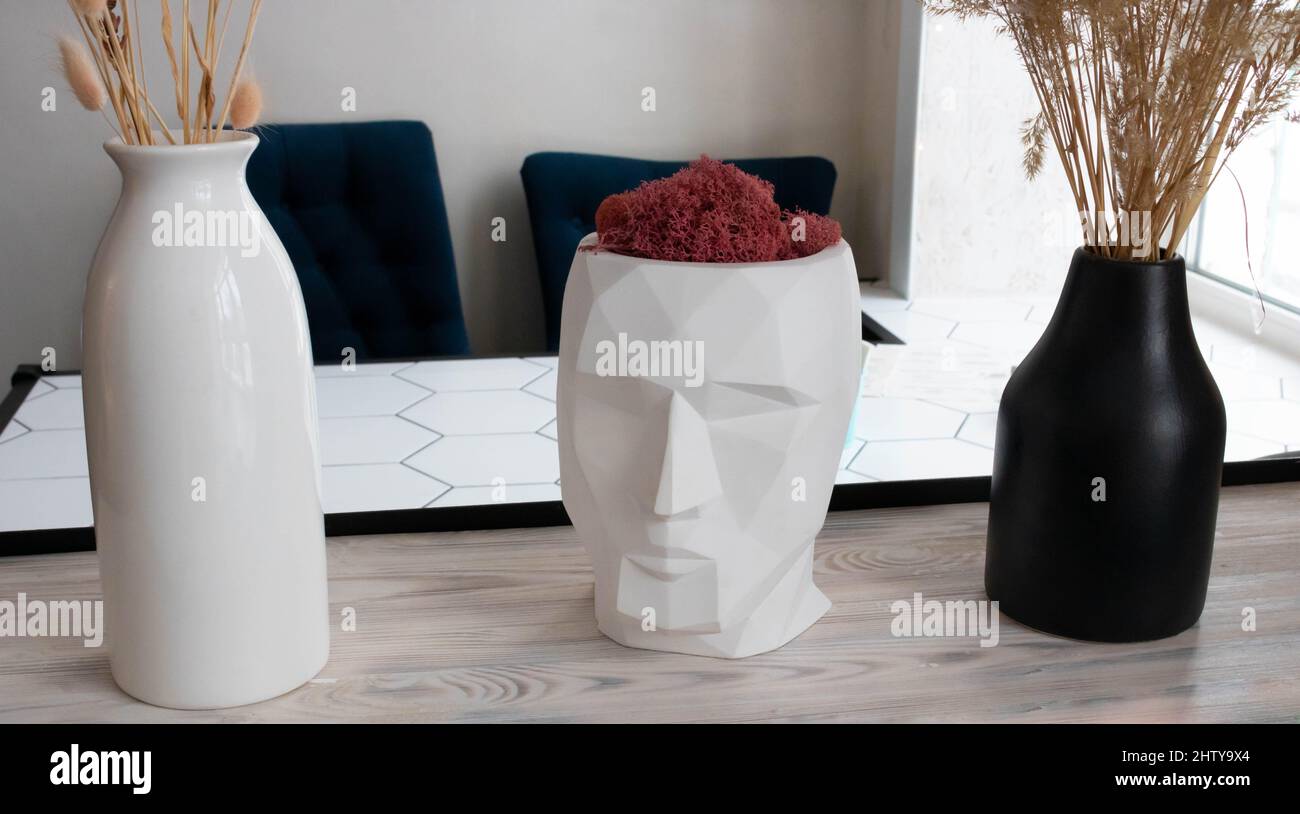 Una scultura bianca della testa di un uomo con una pianta rossa si erge su una mensola. Foto Stock