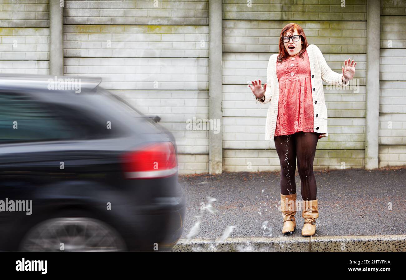 Stare in piedi nel posto sbagliato. Una giovane donna coperta d'acqua dopo che una macchina ha guidato oltre e la ha spruzzata. Foto Stock