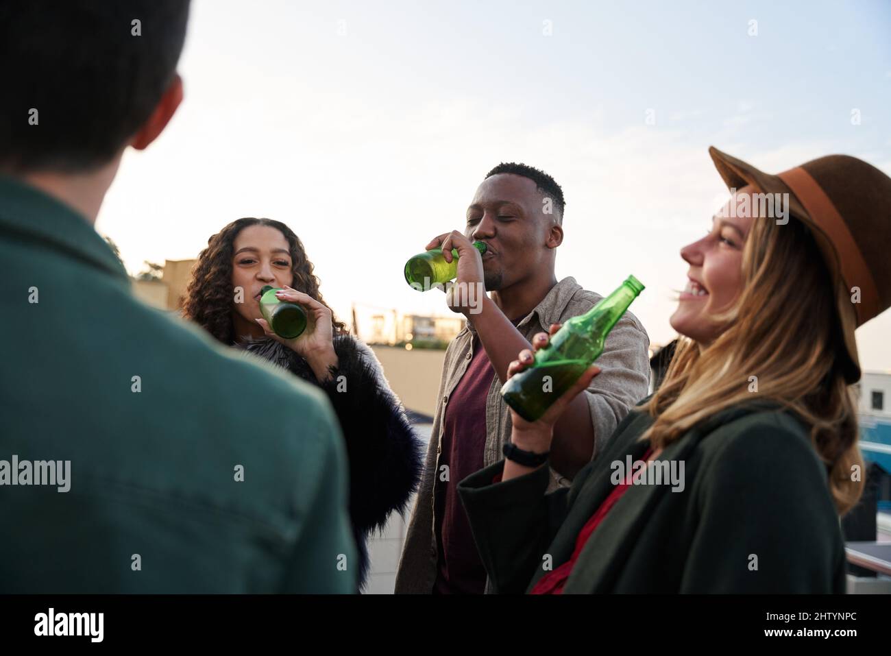 Gruppo multiculturale di giovani adulti che ridono con bevande sul balcone di una terrazza panoramica della città. Foto Stock