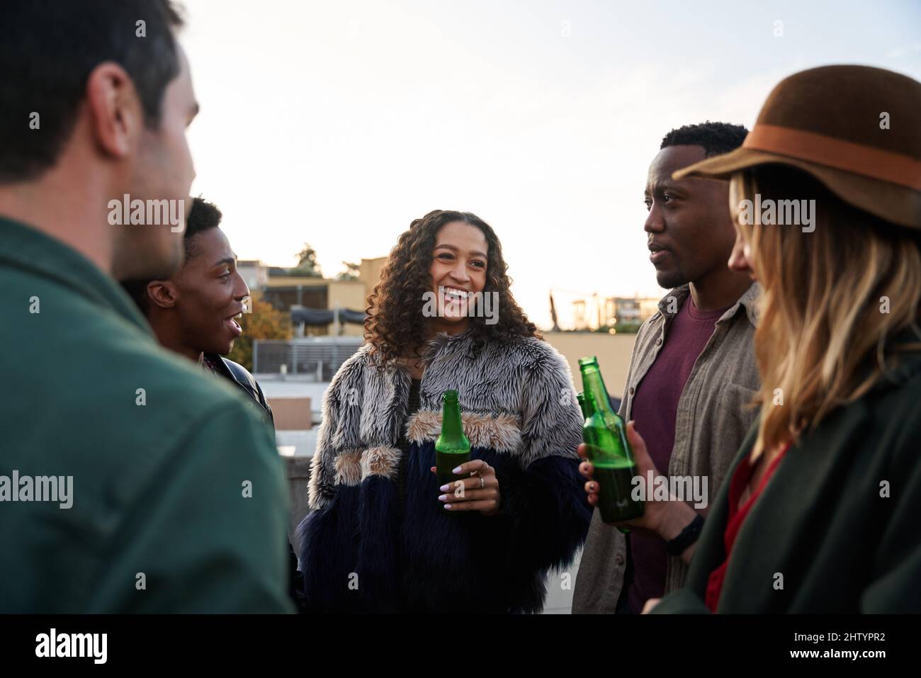 Gruppo multiculturale di giovani adulti sorridenti con bevande sul balcone di una terrazza panoramica della città. Foto Stock