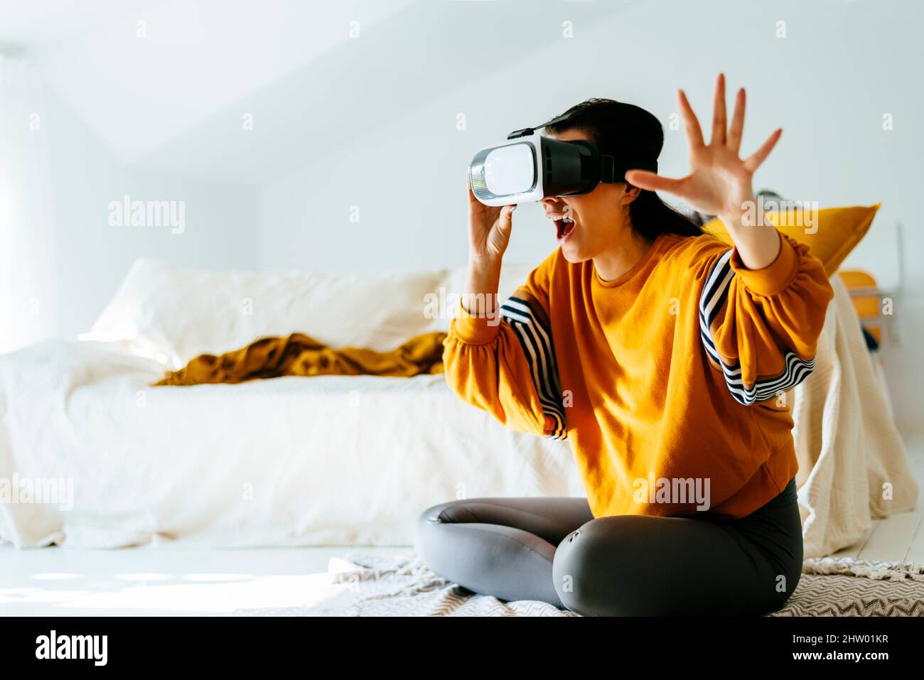 Donna eccitata di abbigliamento casual che indossa occhiali VR per realtà virtuale in salotto. Tendenza futura utilizzando il dispositivo di occhiali per la realtà virtuale per la videoga Foto Stock