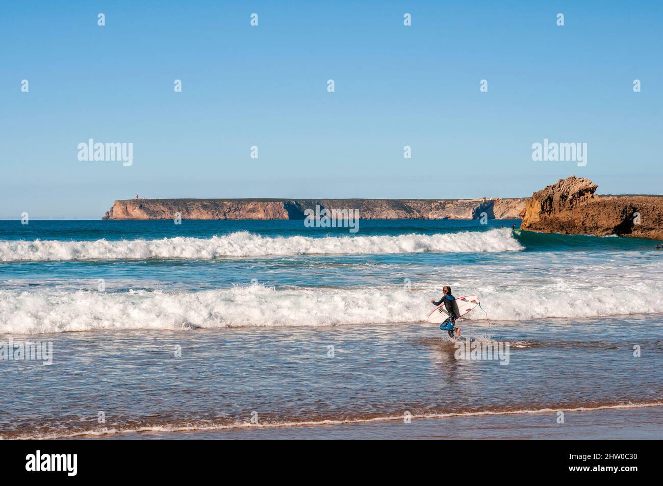 Surfista che entra in acqua con il loro bordo sulla bella spiaggia portoghese Foto Stock