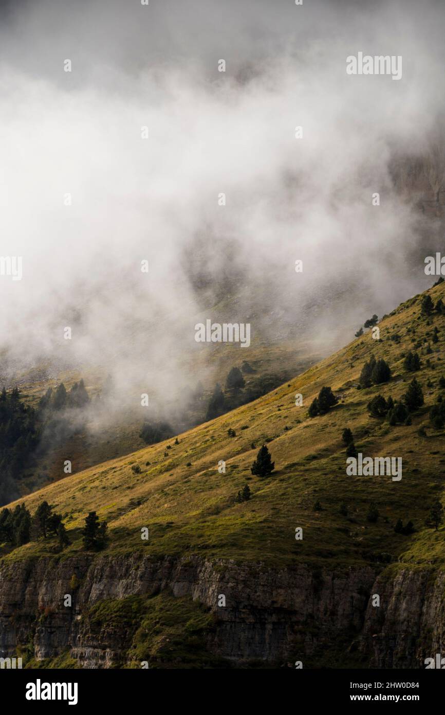 Pendii di montagna tagliati in verticale coperti di erba verde e vegetazione sotto le nubi nubi nebbie Foto Stock