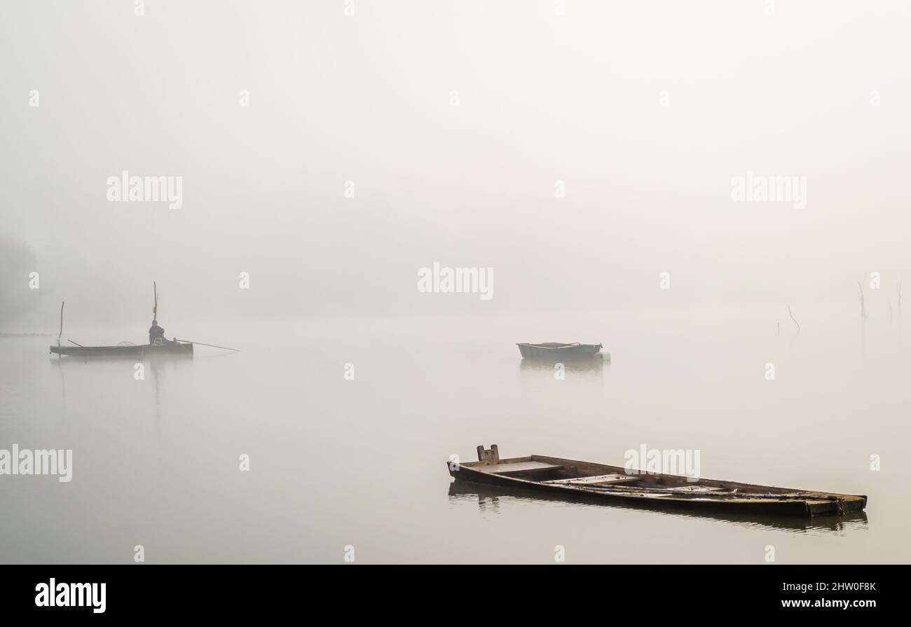 Una barca di legno dimenticata nell'acqua dello stagno, coperta di nebbia. Foto Stock