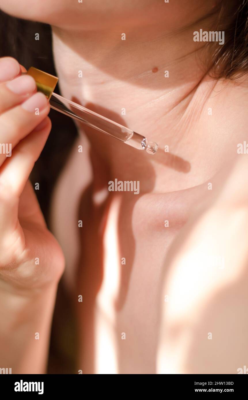 Una donna applica olio al suo corpo. Una goccia di olio essenziale gocciola da una pipetta sulla spalla di una donna. Siero corporeo. Procedure cosmetiche Foto Stock
