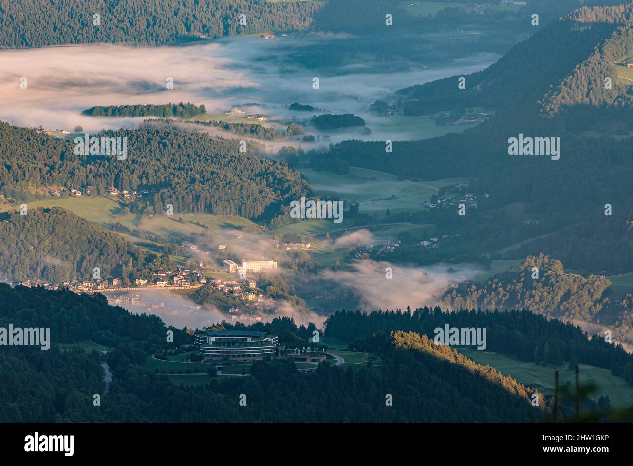 Germania, Baviera, alta Baviera, Berchtesgaden, Obersalzberg, Sunrise nebbia sopra il lussuoso hotel Kempinski e campo da golf che sostituisce il Berghof, l'ex quartier generale di Hitler durante la seconda guerra mondiale, la città di Berchtesgaden nella pianta dello sfondo Foto Stock