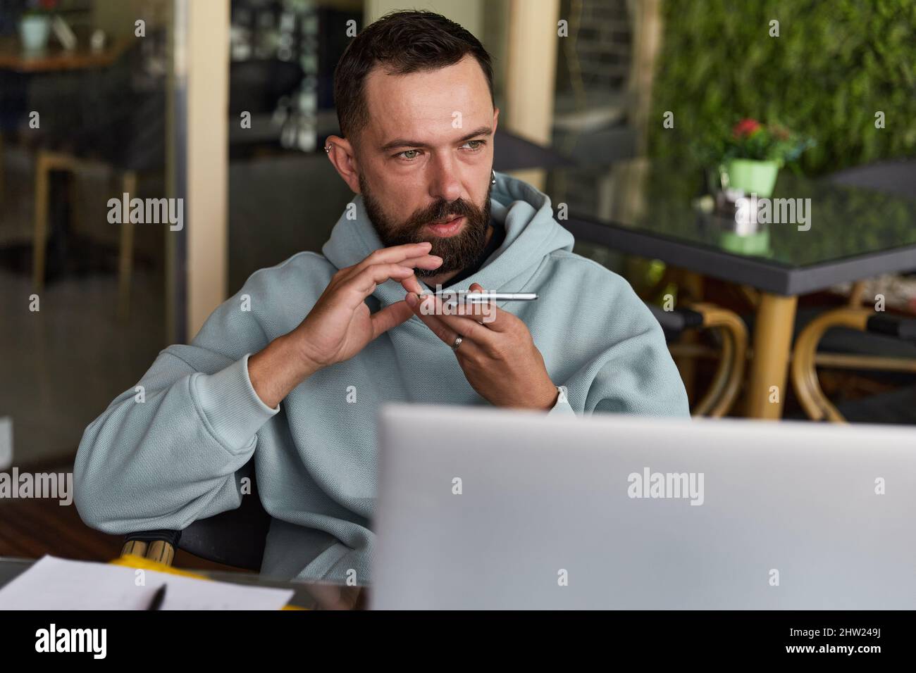 Il giovane uomo adulto premuroso in abiti casual in un caffè registra messaggi audio Foto Stock