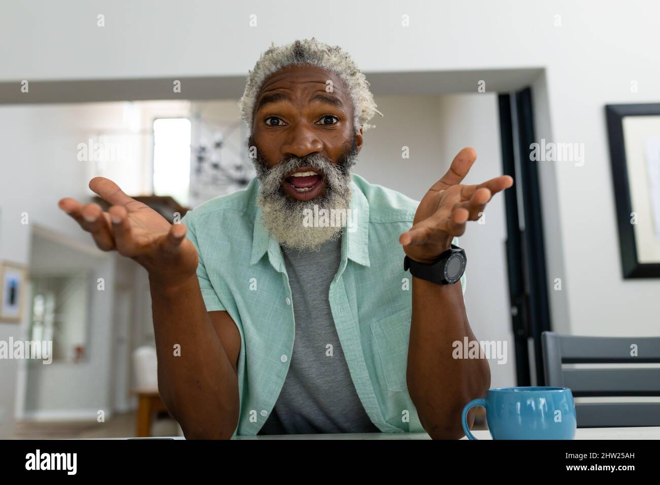 Ritratto di sorprendo uomo anziano afroamericano gesturing mentre si siede in soggiorno a casa Foto Stock