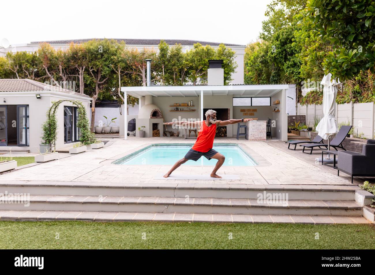 L'uomo anziano afroamericano che pratica il guerriero posa yoga a bordo piscina Foto Stock