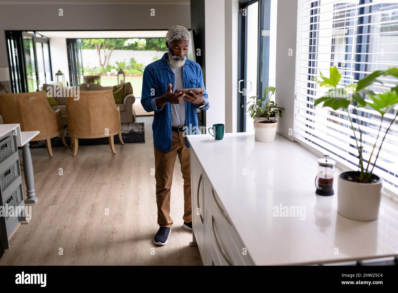 Un uomo afro-americano che tiene il tablet digitale in piedi nel soggiorno di casa Foto Stock