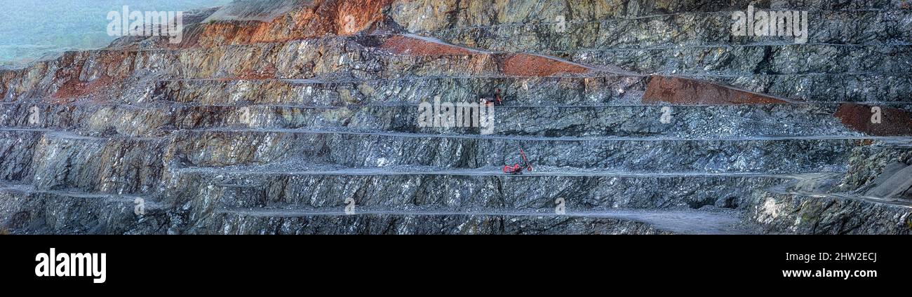 Parete a gradini della cava della diabase con due macchine da perforazione rosse, ampio panorama che mostra diversi strati di pietra Foto Stock