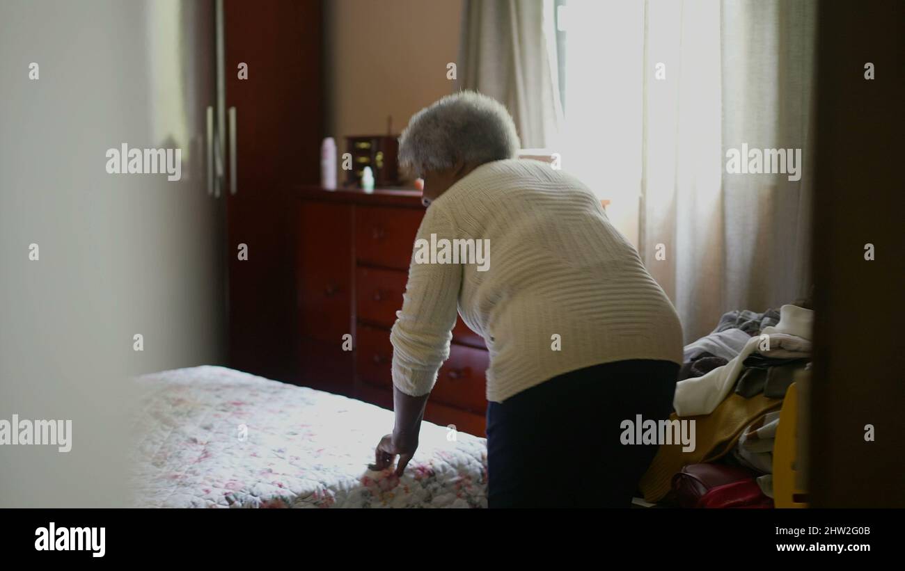 Una donna africana anziana riordinare la stanza togliendo i vestiti dal letto organizzando i lavori domestici Foto Stock