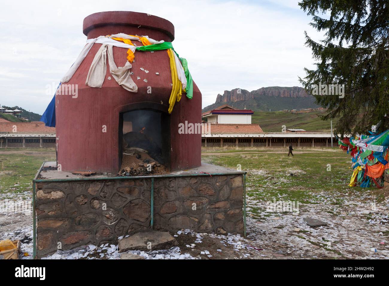 Inceneritore con contenuti brucianti vicino agli edifici del tempio e al tempio principale di Kerti o Kriti Gompa a Langmusi, sulla pianura tibetana in Cina, Repubblica popolare Cinese. Confine delle province di Sichuan e Gansu. Cina. PRC. Il terreno è coperto da note di preghiera stampate. (125) Foto Stock