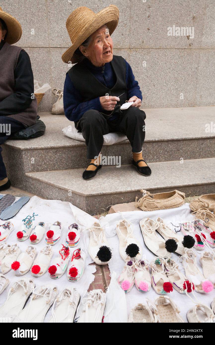 Anziana anziana anziana donna, oap, pensionato, e venditore di scarpe da  marciapiede venditore di strada, che vende calzature, biancheria e sandali  e pantofole di cotone, sul marciapiede a Tianshui, provincia di Gansu,